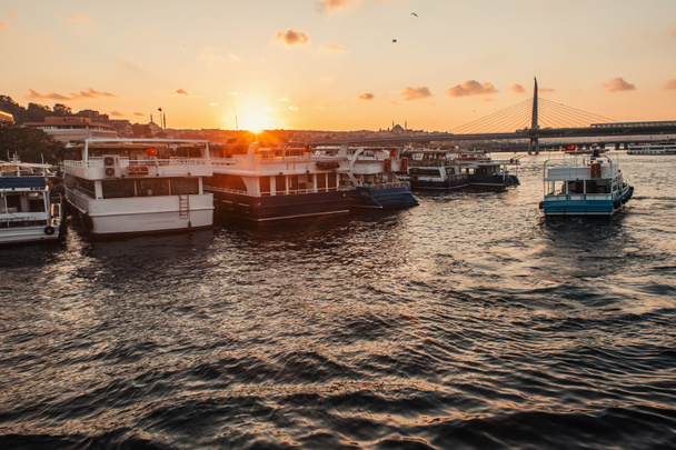 Швартованные лодки рядом с береговой линией и мостом метро Golden horn на фоне заката, Турция  - Фото, изображение