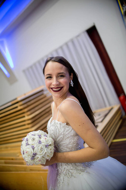 Un disparo vertical de una feliz novia sonriente con un vestido de lujo y sosteniendo un ramo - Foto, imagen