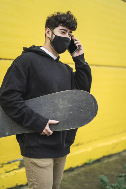 A young European male holding a skate and cheerfully talking on a phone - Фото, зображення