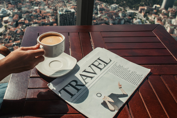 καλλιεργημένη άποψη του ανθρώπου κρατώντας καφέ κοντά σε ταξιδιωτική εφημερίδα στο καφέ με εναέρια θέα της Κωνσταντινούπολης - Φωτογραφία, εικόνα