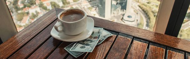 cup of coffee and dollars on wooden table in cafe with aerial view of Istanbul, banner - Photo, Image