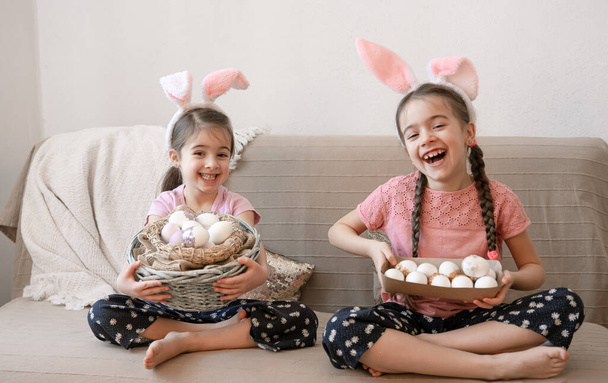 Kis boldog nővérek nyuszifülekkel, húsvéti tojással. Húsvéti ünnepi koncepció. - Fotó, kép