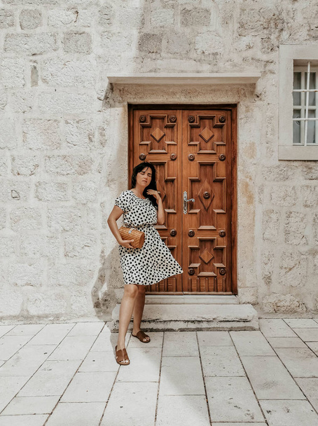 A confident Caucasian woman in a polka-dotted flowy dress posing against a decorative old door - Fotografie, Obrázek