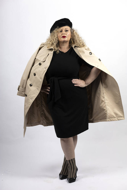 A vertical shot of a mature plus-size female model in a black dress and coat on a white background - Foto, Imagen