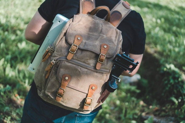 A shallow focus of an adult male with a modern brown backpack with a laptop in itwalking in a park - Foto, afbeelding