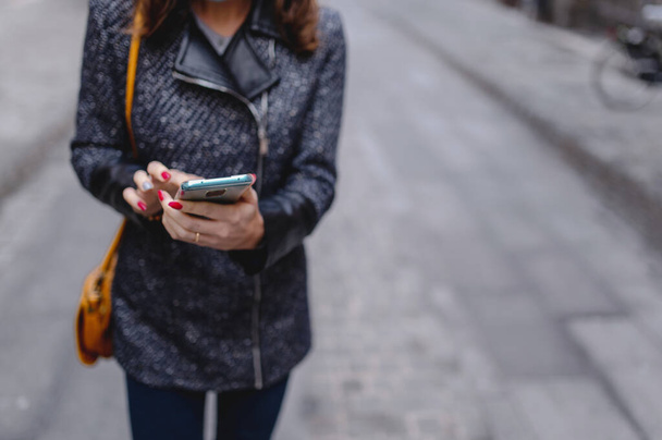 A closeup shot of a woman's hands scrolling on her phone in gloomy weather with blurred background - Foto, afbeelding