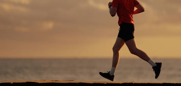 Un hombre en forma corriendo a lo largo de la orilla del océano por la mañana. Hombre sano trotando en la playa - Foto, Imagen