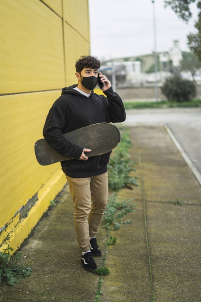 A young European male holding a skate and cheerfully talking on a phone - Photo, image