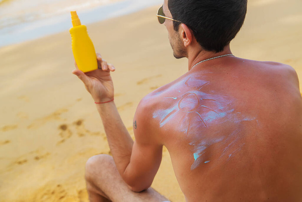Un hombre en la playa con protector solar en la espalda. Enfoque selectivo. Viajes. - Foto, Imagen