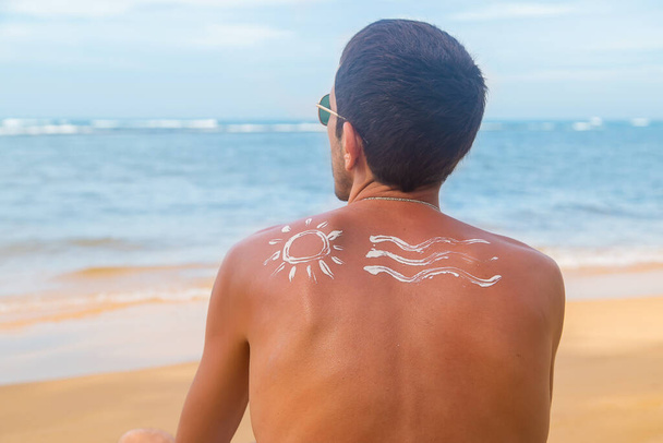 Muž na pláži s opalovacím krémem na zádech. Selektivní soustředění. Cestování. - Fotografie, Obrázek