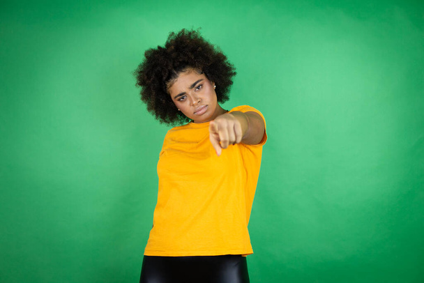 Afroamerikanerin trägt orangefarbenes Hemd über grünem Hintergrund und zeigt mit dem Finger in die Kamera und zu Ihnen, selbstbewusste Geste, die ernst wirkt - Foto, Bild