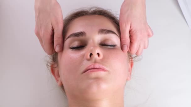 Massage facial soin de beauté. Gros plan d'une jeune femme visage couché sur le dos, se faire masser le visage levant, pincer et rouler technique - Séquence, vidéo