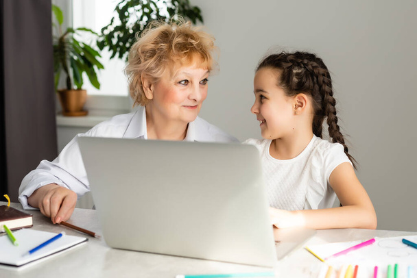 Babička učí vnučku pomocí počítače. Starostlivý starý učitel pomáhá dívce studovat a dělat domácí úkoly na notebooku doma, soukromá lekce - Fotografie, Obrázek