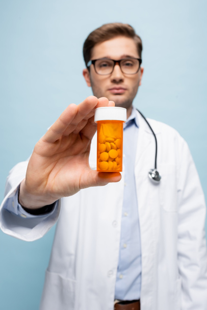 Flasche mit Medikamenten in der Hand des Arztes auf verschwommenem Hintergrund isoliert auf blau - Foto, Bild
