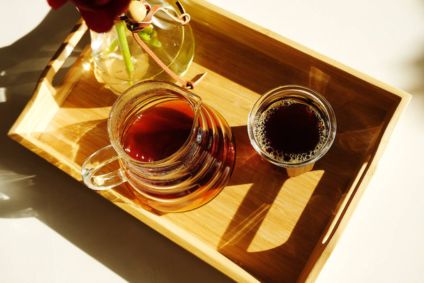 Frisch gebrühter schwarzer Kaffee wird auf einem Bambustablett auf einem sonnenbeschienenen weißen Tisch serviert. Ansicht von oben - Foto, Bild