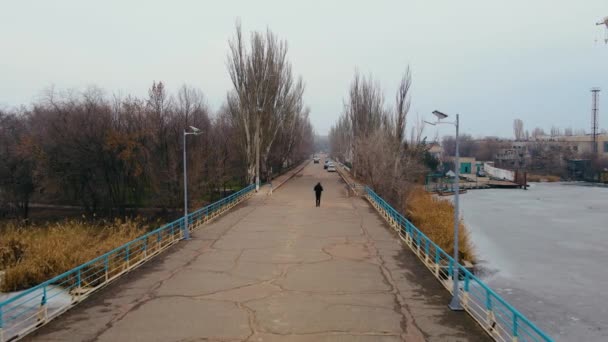 Magányos ember sétál a gyalogos hídon kis napelemekkel vagy akkumulátorokkal a kikötőben, kevés utassal a járdaszegélyen. - Felvétel, videó