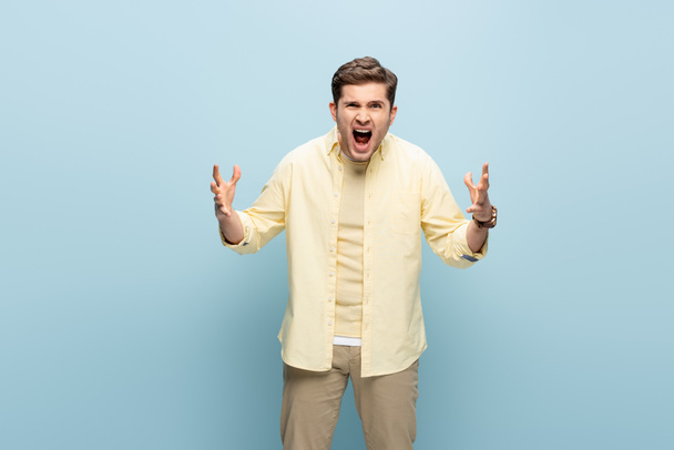 Wütender junger Mann schreit und gestikuliert auf blauem Grund - Foto, Bild