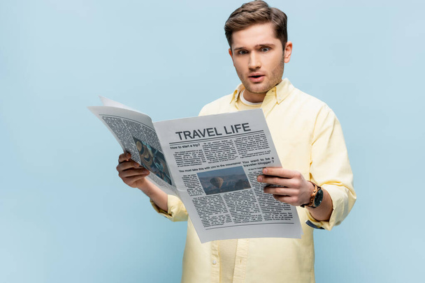 έκπληκτος άνθρωπος που διαβάζει ταξιδιωτική εφημερίδα απομονωμένη στο μπλε - Φωτογραφία, εικόνα