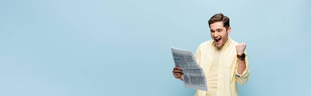 joven emocionado en camisa leyendo periódico aislado en azul, pancarta - Foto, Imagen