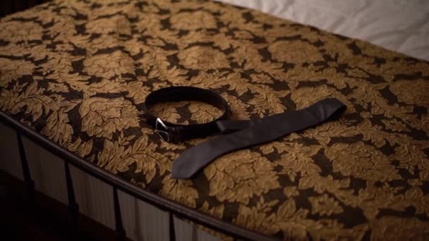 結婚式の準備中にホテルのベッドの上に革ベルトとネクタイが横たわっています  - 映像、動画