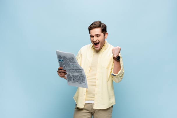 joven emocionado en camisa leyendo el periódico en azul - Foto, Imagen