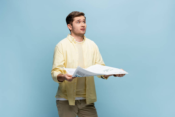 scioccato giovane uomo in camicia tenendo giornale su blu - Foto, immagini