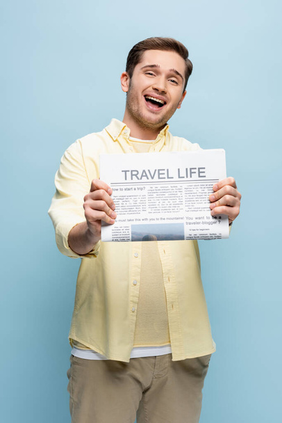 κατάπληκτος νεαρός άνδρας με πουκάμισο κρατώντας ταξιδιωτική εφημερίδα απομονωμένη στο μπλε - Φωτογραφία, εικόνα
