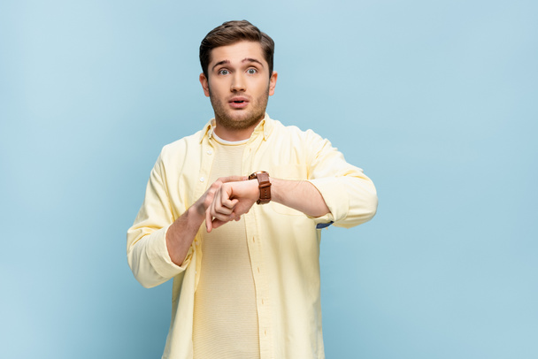 hombre preocupado en camisa amarilla con reloj de pulsera a mano aislado en azul - Foto, Imagen