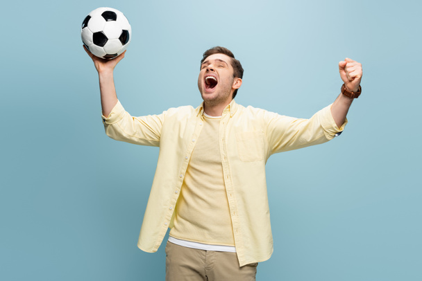 Sportfan im gelben Hemd hält Fußball in der Hand und feuert Blau an - Foto, Bild