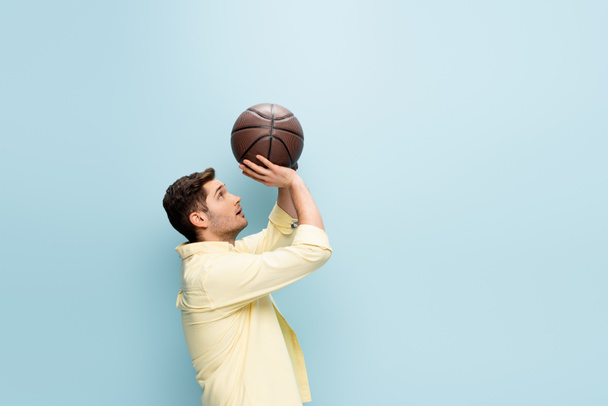 vista laterale dell'uomo in camicia gialla che lancia basket su blu - Foto, immagini