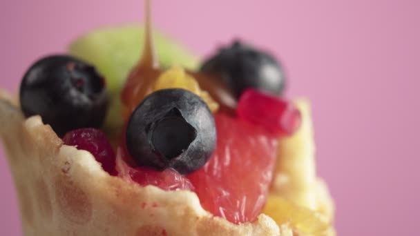 Vers en sappig fruitsalade met bosbessen in een wafelmand op een roze achtergrond, macro shot. Heerlijke zelfgemaakte fruit en bessen mix, gieten met karamel topping. Veganistisch voedselconcept. - Video