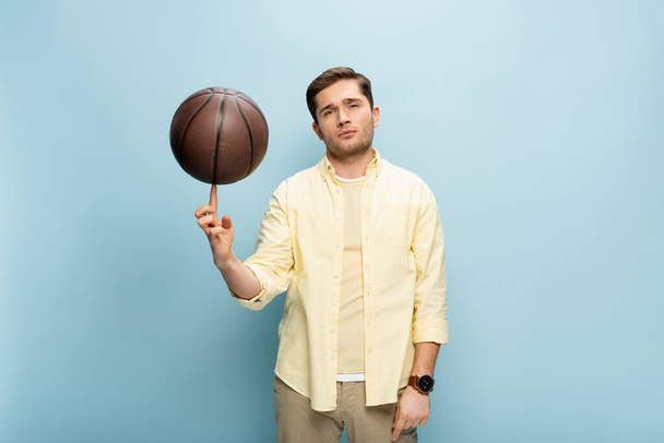 speler in geel shirt spinnen basketbal op vinger op blauw - Foto, afbeelding