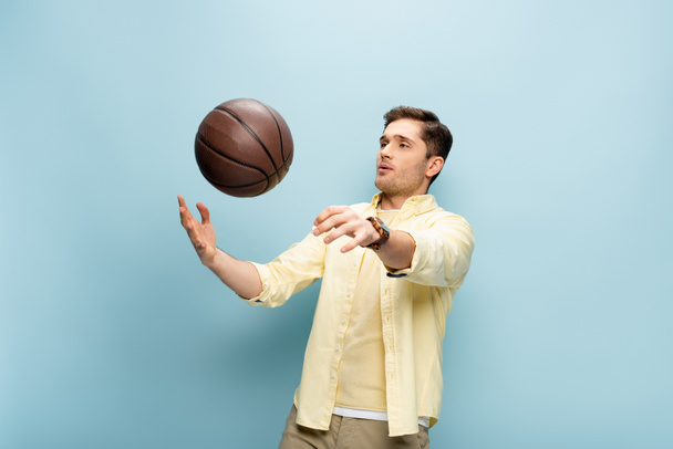 uomo in camicia gialla che lancia pallacanestro in aria su blu - Foto, immagini