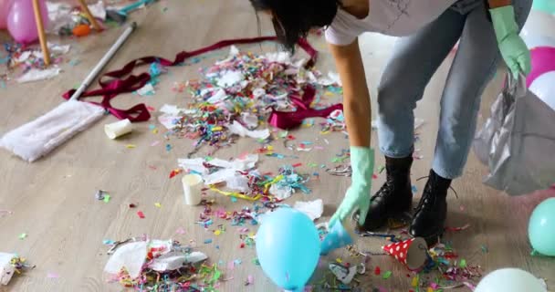 Kobieta sprzątanie bałaganu podłogi w pokoju po imprezie, usuwa śmieci z podłogi, jednorazowe kubki w torbie, rano po imprezie uroczystości, prace domowe, sprzątanie - Materiał filmowy, wideo