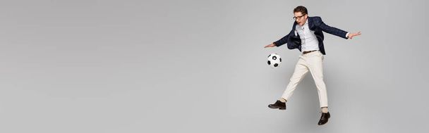 full length του χαρούμενου επιχειρηματία που παίζει ποδόσφαιρο, ενώ αιωρείται σε γκρι, banner - Φωτογραφία, εικόνα