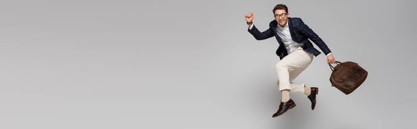 full length of cheerful businessman with leather bag levitating on grey, banner - Photo, Image