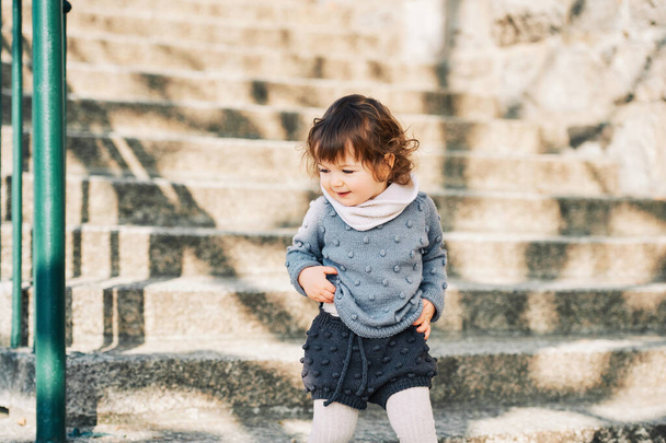 Venkovní portrét rozkošné batolata dívka kráčející po schodech, dítě 1 - 2 roky šplhání po ulicích města, na sobě pletenou sadu svetru a kraťasů - Fotografie, Obrázek