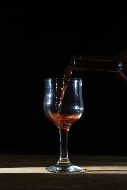 Hausgemachter Rotwein wird in ein Glas auf dunklem Hintergrund gegossen. Ein Glas Rotwein auf schwarzem Hintergrund. Alkoholische GetränkeHausgemachter Rotwein wird in ein Glas auf dunklem Hintergrund gegossen. Ein Glas Rotwein auf schwarzem Hintergrund. Alkoholisches Getränk - Foto, Bild