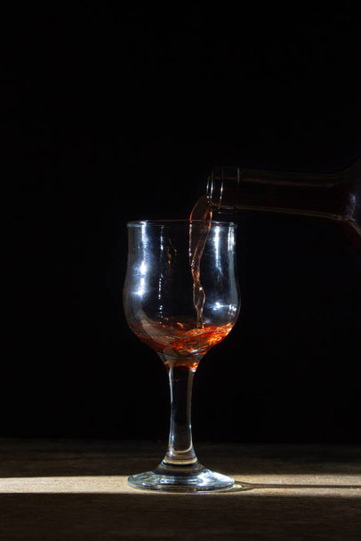 Homemade red wine is poured into a glass on a dark background. Glass of red wine on a black background. Alcoholic beverage - Photo, Image