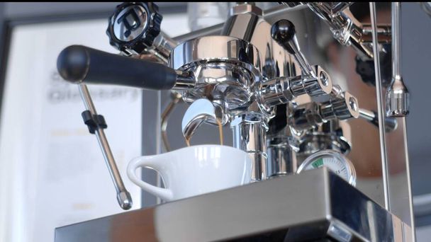 Het extraheren van espresso uit een groep stalen koffiezetapparaat in een witte keramische beker. Laaghoekige foto van hoge kwaliteit. - Foto, afbeelding