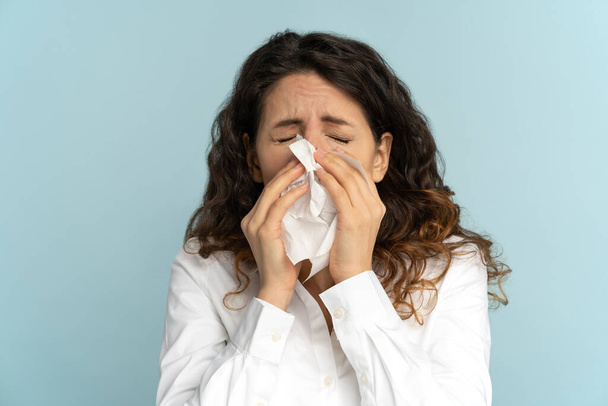 Kobieta kichająca do papierowej tkanki, cierpiąca na sezonową alergię, nieżyt nosa, izolowana w studio. - Zdjęcie, obraz