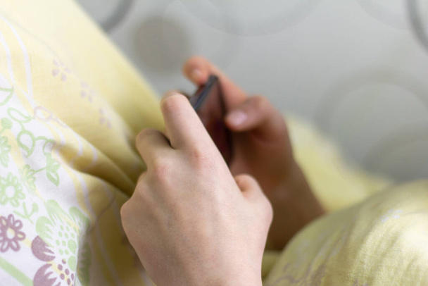 The phone is in the hands of a teenager lying in bed. - Photo, Image