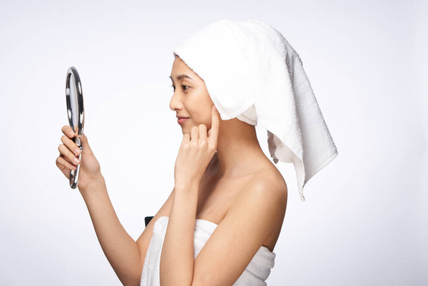 woman of asian appearance after shower looks in the mirror skin care light background - Foto, Imagem