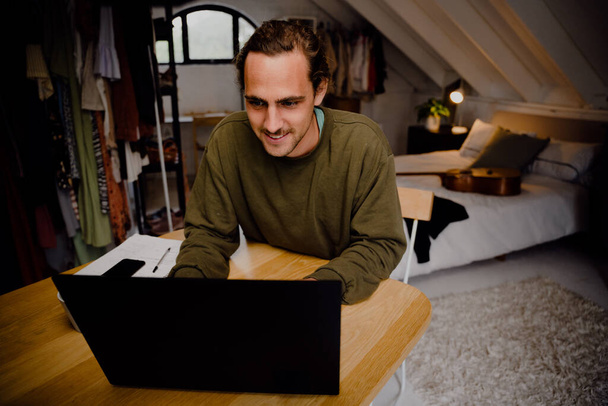 Caucásico estudiante masculino estudiando desde casa escribiendo en el ordenador portátil sentado en el escritorio en casa oficina - Foto, Imagen