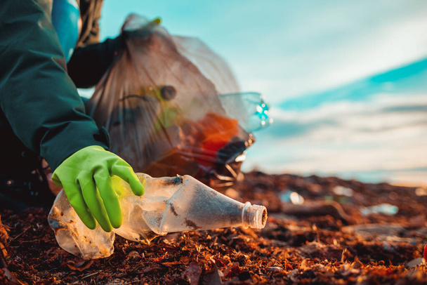 Un travailleur en gants de caoutchouc recueille une bouteille en plastique sur une plage. Gros plan de la main. Le concept du Jour de la Terre et le problème de l'écologie. - Photo, image