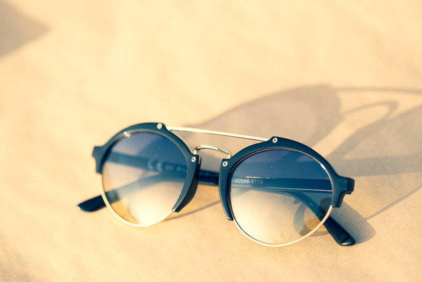 Солнечные очки с круглыми линзами снимают на открытом воздухе в солнечный день крупным планом. Селективный фокус - Фото, изображение