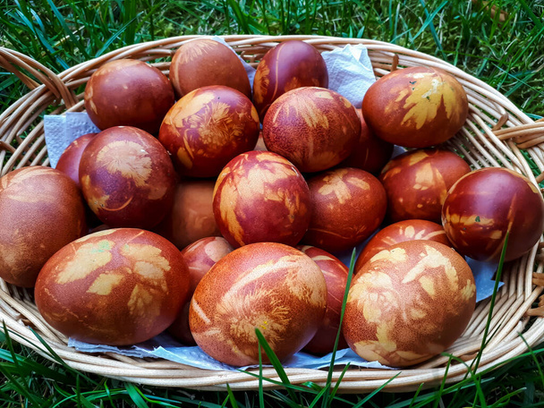 Velikonoční vejce Zdobená přírodními rostlinami a květy květin a vařená v cibuli Loupaná v tkané koši v zelené trávě. Tradiční způsob, jak vytvořit vzor rostlin na hnědých vejcích - Fotografie, Obrázek