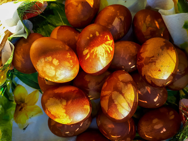 Ostereier dekoriert mit natürlichen Pflanzen und Blüten und gekocht in Zwiebelschalen in geflochtenem Korb im Sonnenlicht. Traditionelle Methode, Muster von Pflanzen auf braunen Eiern zu erzeugen - Foto, Bild