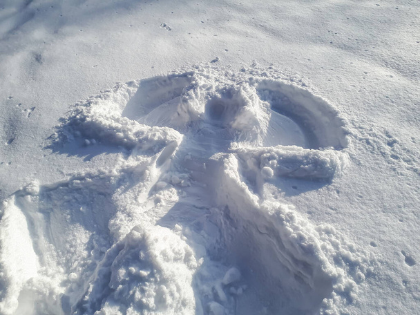 Conception d'ange des neiges réalisée dans la neige fraîche et profonde, en étant couché sur le dos et en déplaçant les bras de haut en bas, et les jambes d'un côté à l'autre en hiver par une journée ensoleillée - Photo, image