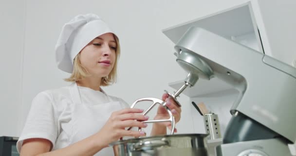 Cukiernik w kuchni restauracji zawiera mieszalnik, Food Processor. Chef Girl Confectioner, Korzystanie z nowoczesnego elektrycznego procesora żywności do mieszania ciasta do pieczenia ciasta lub ciasteczka. - Materiał filmowy, wideo
